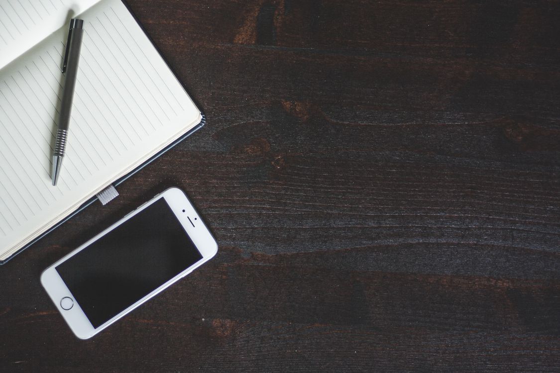 Smartphone on a dark wood desk next to a notebook and pen