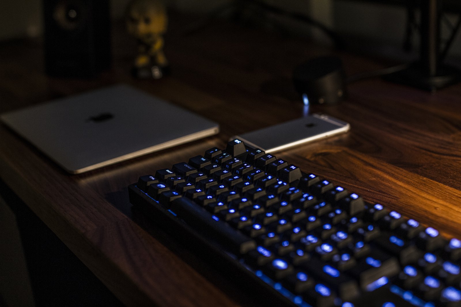 Backlit mechanical keyboard on a wooden desk beside a phone and tablet